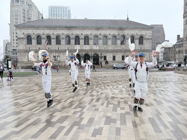 Newtowne Morris performing Fieldtown Dearest Dickie on Copley Plaza across from the Boston Public Library, two lines of dancers in whites, suspenders, and blue caps facing the camera and waving their hankies.